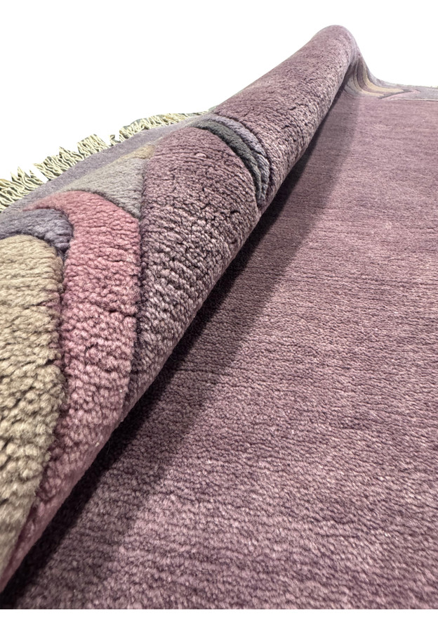 Rolled corner of the round Nepali rug revealing dense wool pile and dusty purple selvage