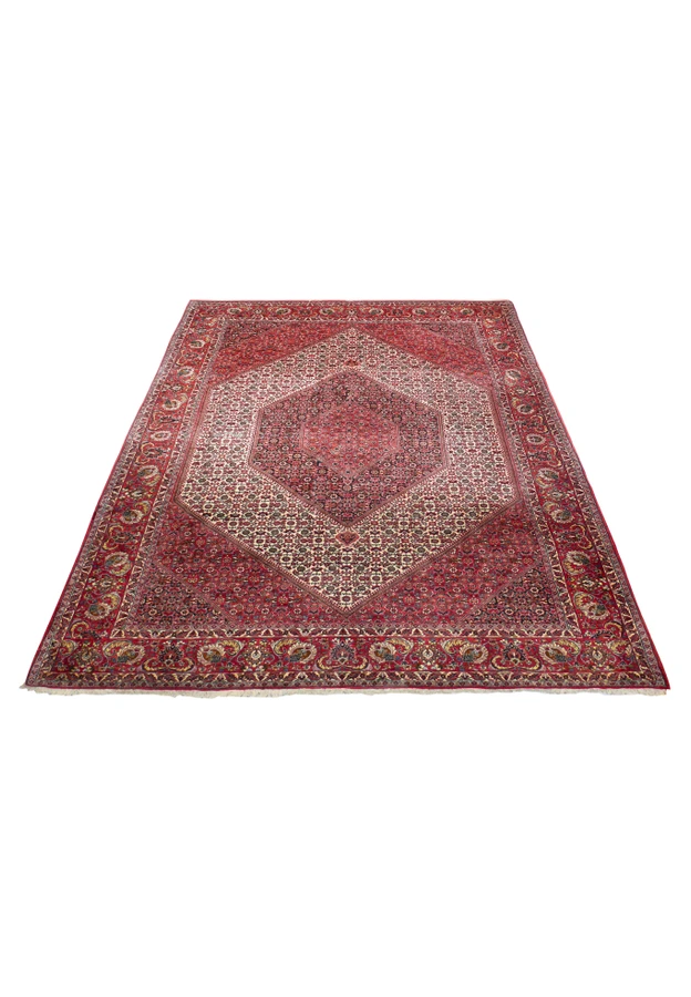 Persian Bijar rug at an angle, warm red field and cream medallion framed by a bold red palmette border