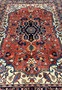 Midfield detail of a geometric Persian Heriz rug showing floral motifs, angular vines, and saturated red background