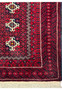 Corner detail of a Persian Baluch rug, focusing on the intricately patterned border and fringed edges