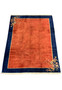 Angled perspective of a modern 10 x 13 Oriental Art Deco rug showing the plush burnt orange field bordered by navy blue with a thin golden line, and the corner with an elaborate floral design.