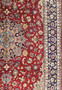 Partial view of a 10 x 15 Persian Isfahan rug laid out to display the harmonious design with a deep crimson field and a navy blue border rich with floral patterns