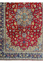 A full view of the entire Persian Isfahan rug, emphasizing the symmetrical design, with a dominant crimson center, intricate floral motifs, and a prominent dark blue border with gold and cream patterns