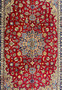 A close-up view of the central part of a Persian Isfahan rug, highlighting the elaborate central medallion and the detailed floral patterns in colors of blue, gold, and white on a red background