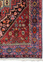 A corner section of a Persian Gholtogh rug, displaying the meticulous detail of the border designs and the transition of colors from the edge to the central area