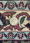 Image showing a quarter placed on the edge of a Bijar Persian rug to give an idea of the scale of the detailed patterns and knotting. The edge showcases the rug's robust border filled with symmetrical patterns in a blend of red, blue, green, and cream colors, alongside the rug's neatly woven fringe.
