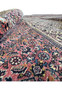 Perspective view of a partially rolled Bijar Persian rug spread across a floor, displaying rich, traditional designs. The visible patterns include a complex array of floral and tribal symbols, predominantly in reds, blues, and beiges, woven tightly to create a durable and heavy fabric