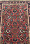 Close-up of the Persian Bijar rug showing the detailed herati pattern design on the red background, bordered by deep indigo edges and intricate floral motifs