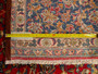 A segment of the Persian Isfahan rug with a measuring tape lying across it, providing a scale reference that highlights the rug's fine knot density and the minuteness of each knotted pile