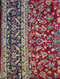 Macro view of the Persian Isfahan rug's border, featuring a navy blue background with a succession of detailed flowers and serpentine vines in contrasting colors of cream, red, and lighter blue tones