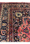 A segment of a Persian Mashad rug showing the elaborate detail of the border and the richly decorated field. The image captures the variety of floral motifs and the vibrancy of the colors, including shades of indigo, blue, pink, and beige, against the salmon pink background of the rug’s center.