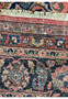Detailed image of the fringe and border of a Persian Mashad rug. The image displays the fine white fringe, which transitions into the intricate border pattern featuring geometric and floral motifs in a rich array of colors such as deep blue, red, and pink on a dark navy background