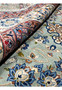 Rolled view of Persian Tabriz rug showing wool pile texture and vibrant blue, beige, and ivory floral details