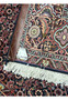 Back corner of Bijar Persian rug displaying handwritten size tag, leather binding, and intricate rust-red floral pattern woven with navy, beige, and light blue.