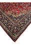 Corner section of Persian Isfahan rug showing navy border, floral blossoms, and ruby red field