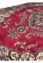 Macro closeup of vintage Persian Tabriz rug showing worn pile, patina, and fine floral outlines against the distressed red field.
