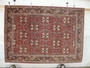 Hanging view of floral Bijar iron rug showing brick red background, ivory palmettes, navy vines, and dense wool texture
