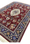 Angled view of Persian Isfahan wool and silk rug showing burgundy field, ivory medallion, and navy floral border