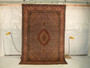 6'6 x 10 Persian Tabriz Mahi rug hanging view with dense Herati pattern and warm rust brown tones