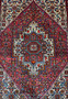 Close-up of the central geometric medallion in a Persian Gholtogh rug, highlighting precise knotting, stepped outlines, rich red tones, and ivory contrast