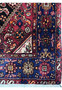 Border close-up of a Persian Gholtogh rug highlighting dense wool weave, bold tribal symbols, navy background, and warm accent colors