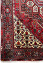 Border detail of a Persian Gholtogh rug with repeating tribal blossoms, navy framing, ivory highlights, and strong contrast against the red field