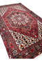 Angled view of a Persian Gholtogh rug emphasizing pile height, saturated red and navy colors, bold medallion presence, and sturdy tribal build