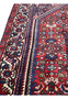 Angled side view of hand-knotted Persian Gholtogh rug highlighting dense wool pile, crisp tribal patterns, and rich red and navy color contrast