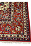 Detailed view of the main border on a Persian Isfahan rug showcasing rich red background, floral arabesques, and precise hand-knotted construction