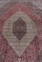 Central field detail of a Persian Bijar iron rug showing dense geometric elements, tight knotting, ivory accents, and rich brick red background