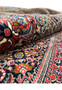 Rolled edge view of a 9x13 Persian Bijar iron rug showing dense wool pile, deep red field, navy blue details, and tightly packed geometric motifs