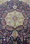 Central medallion of Persian Tabriz rug with ivory, light blue, burgundy, and gold tones set on a deep navy background