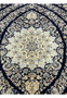 Detailed medallion of a Persian Nain 6 La rug with intricate floral motifs woven in silk and kork wool on a navy background