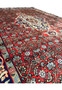 Angled view of a Persian Sarough rug revealing pile texture, brick red field saturation, and finely articulated floral motifs