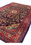 Persian Mahal rug shown from angled view with navy field, red borders, large floral vines, and central ivory medallion, thick wool pile texture visible