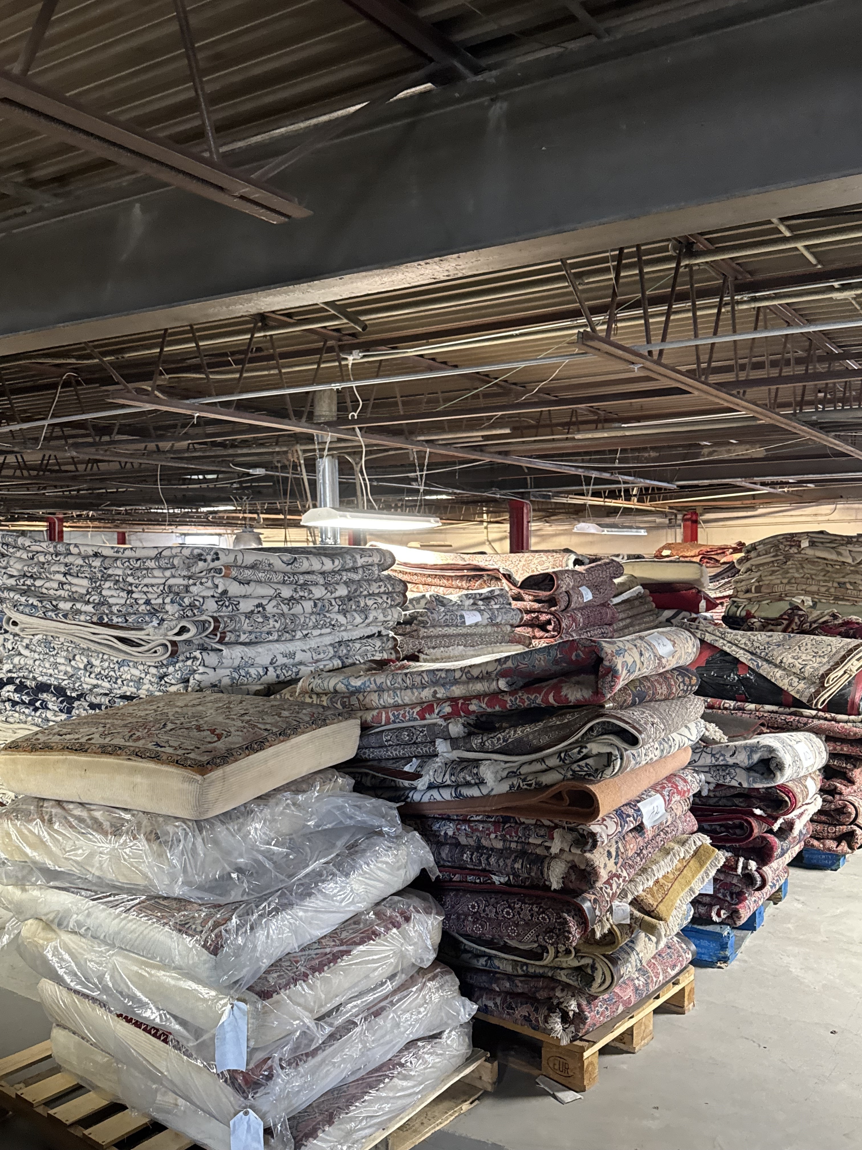 Stacks of folded and rolled Persian rugs filling a warehouse aisle at Rugs.net