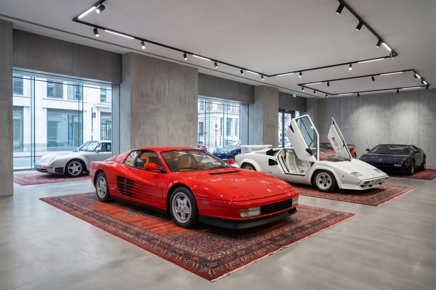 A Ferrari Testarossa, a Lamborghini Countach, a Porsche 959 and a BMW M1 in a concrete showroom, each standing on its own hand-knotted Persian rug