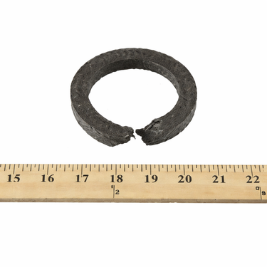 Broken braided graphite packing ring used for industrial pump sealing applications, shown against a measurement ruler for size reference