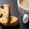 Cup of coffee with two almond biscotti cookies on a dark slate surface