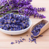 Bowl and wooden scoop filled with dried lavender buds on wooden surface