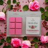 Vanilla Rose wax melts package surrounded by fresh pink roses and small red berries on a floral background.