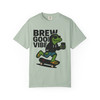 “Bay green tee featuring Bert the gecko riding skateboard with steaming coffee, bold distressed text ‘Brew Good Vibes,’ Gecko Skate Crew Tee by Coo Coo’s Coffee.”
