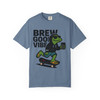 “Blue Jean tee showing gecko mascot Bert skateboarding in hoodie and sunglasses while sipping coffee, text ‘Brew Good Vibes,’ Gecko Skate Crew Tee by Coo Coo’s Coffee.”