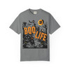“Grey tee showing witch flying across the moon, haunted house, pumpkins, and slogan ‘Boo Life,’ Boo Life Tee by Coo Coo’s Coffee.”