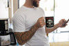 Bearded man in white t-shirt checking his phone while drinking from the Fuel: Coffee skull motor mug.