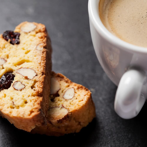 Cup of coffee with two almond biscotti cookies on a dark slate surface