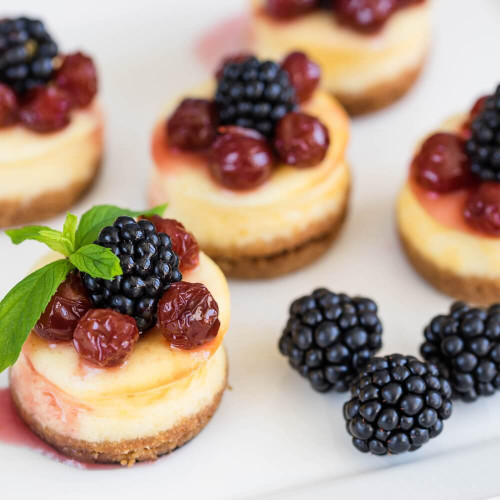 Mini cheesecakes topped with blackberries and cherries on a white surface, showcasing the dessert inspiration behind the Black Raspberry Cheesecake Wax Melt fragrance.