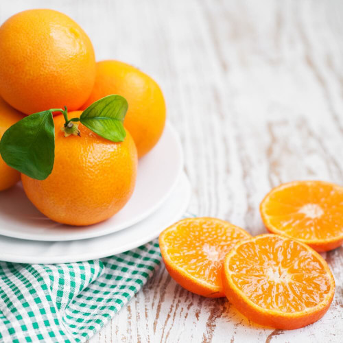 Fresh whole and sliced tangerines on a wooden surface with green leaves, showcasing the fruity inspiration behind Tangerine Delight Wax Melt.