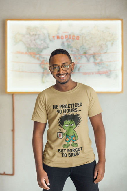 "Man wearing Practice Makes Exhausted – Frazzled Bert Tee by Coo Coo’s Coffee in mustard yellow, standing in front of world map wall art. Funny coffee graphic shirt with frazzled gecko Bert holding a mug. Casual, playful style for coffee lovers."