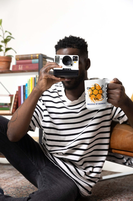Man sitting on the floor taking a photo while holding the Caffeine Cyclone Molecule of Madness coffee mug